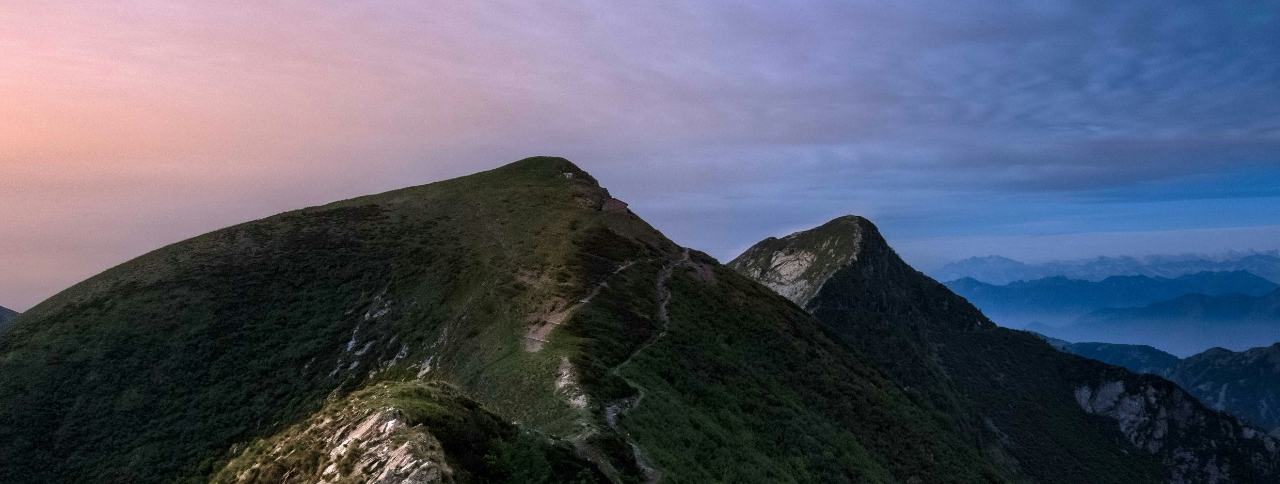 Mountain ridge at dawn with a winding path and a clear sky overhead