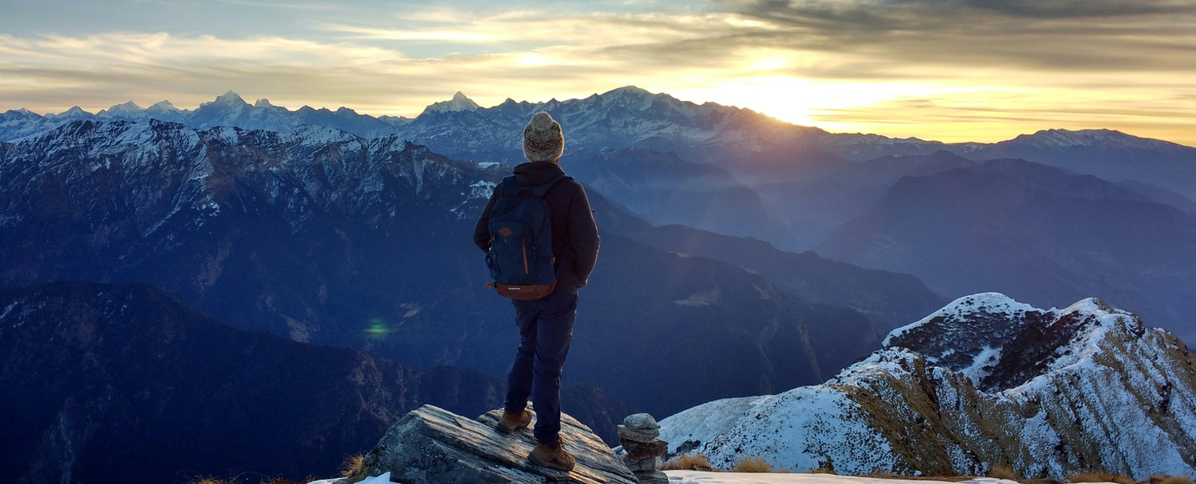 Person standing on a snowy mountain summit at sunrise.