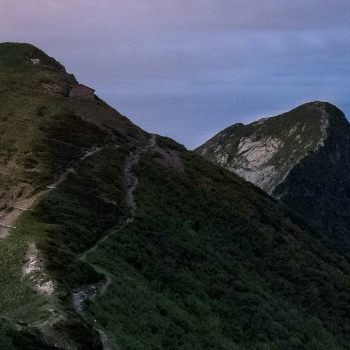 Mountain ridge at dawn with a winding path and a clear sky overhead